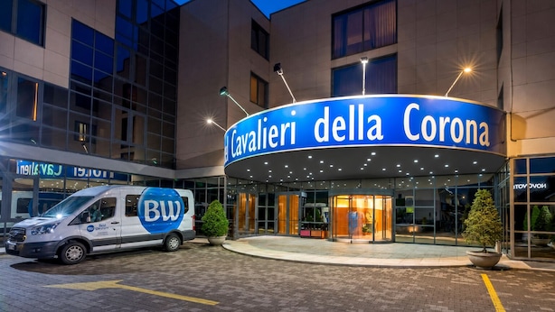 Een hotelingang met een bord waarop 'Cavalieri della Corona' staat, een bestelwagen met 'BW Best Western'-branding en een moderne gevel.