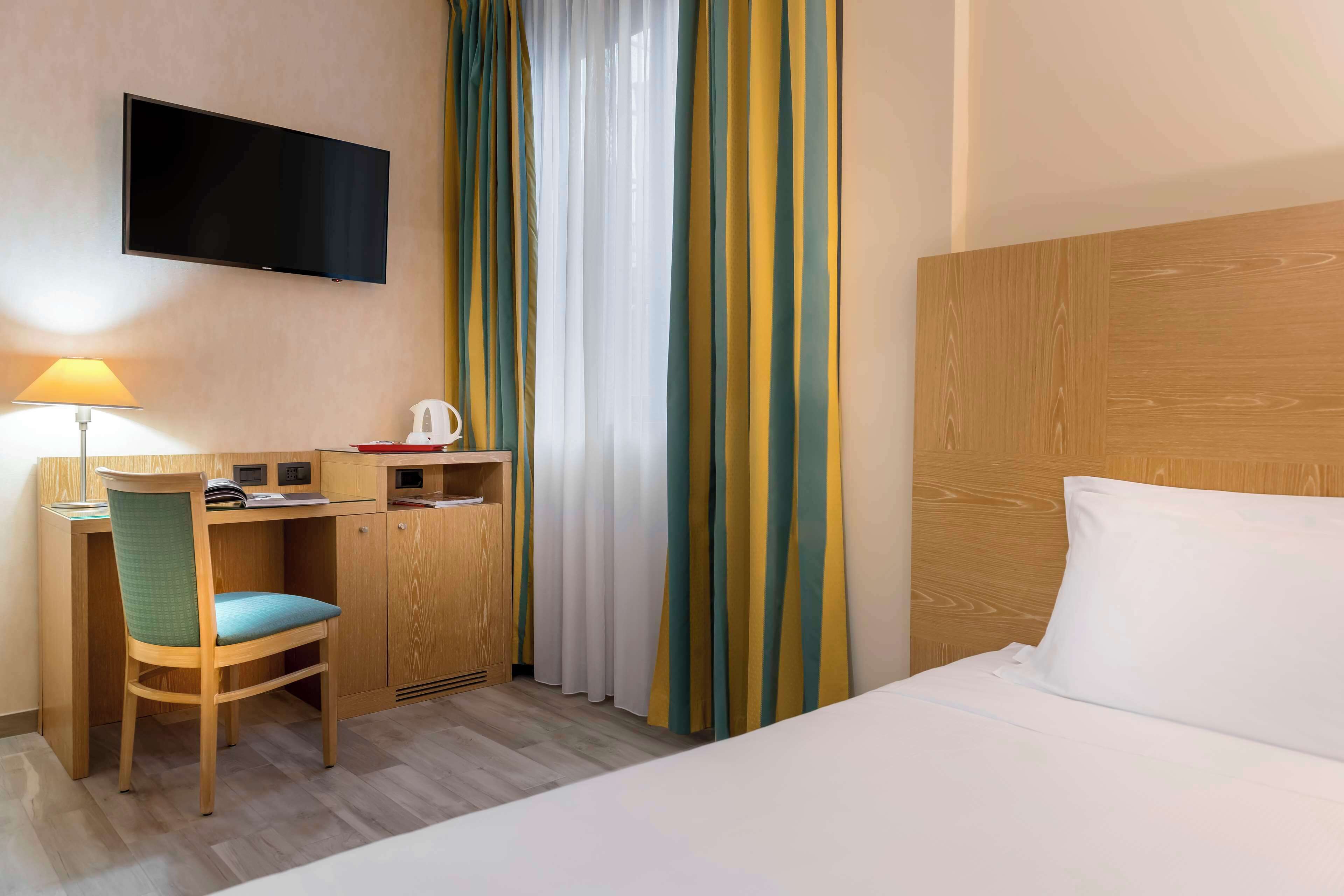 Une chambre d’hôtel avec un lit, un bureau et une chaise, une télévision et des rideaux.