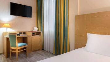 Una camera d'albergo con un letto, una scrivania con sedia, una televisione e tende.