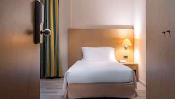 A hotel room with a wooden headboard, a bed with white bedding, a bedside lamp, and a wooden nightstand.