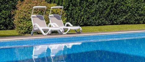 A swimming pool with two white lounge chairs and a hedge in the background.