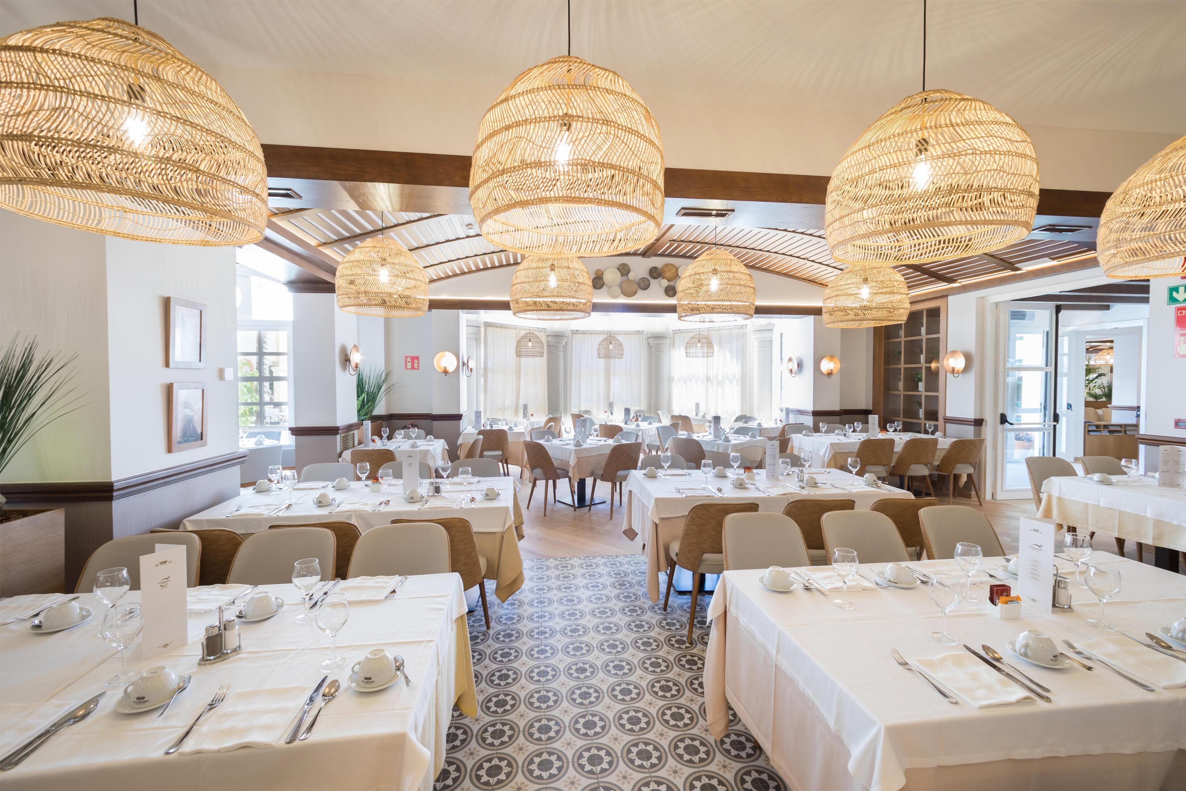 A restaurant with round tables, wicker pendant lighting, and a patterned floor.