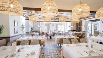 A restaurant with round tables, wicker pendant lighting, and a patterned floor.