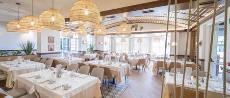 Un restaurante espacioso con varias mesas, lámparas colgantes de mimbre y vistas al exterior.