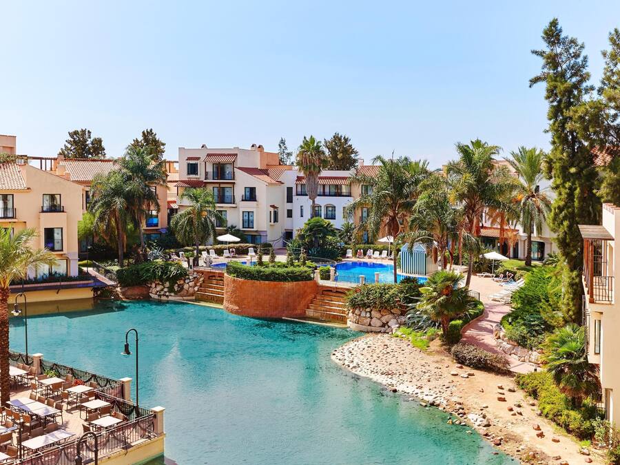 Un resort con piscina central, varias edificaciones y palmeras.