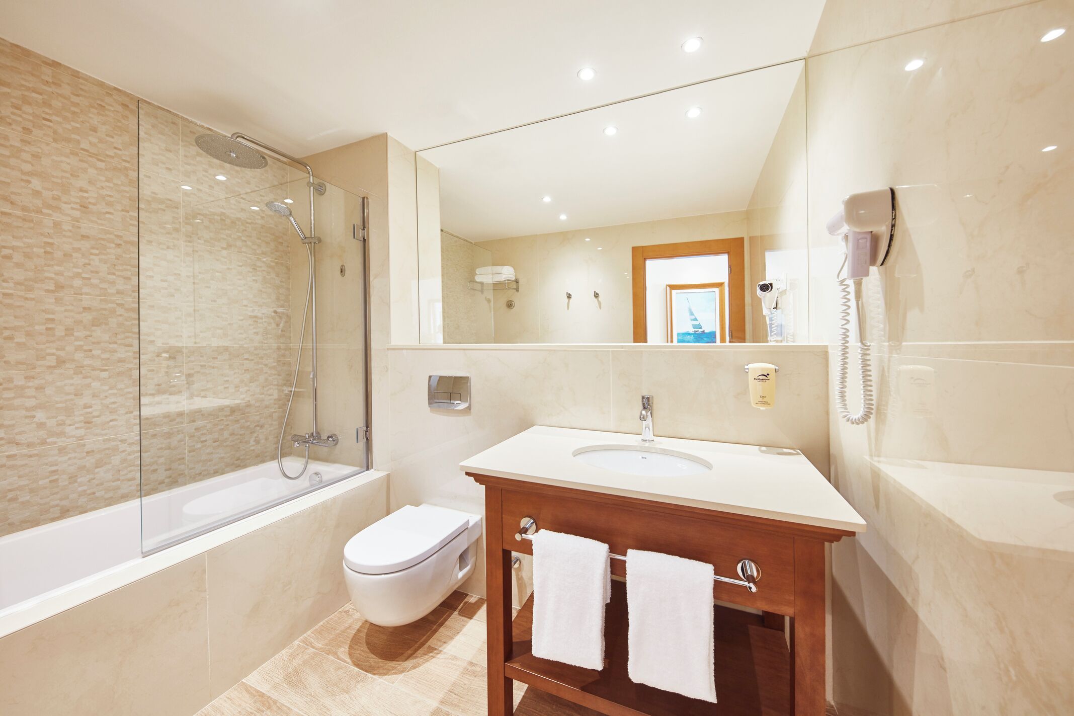 Un baño moderno con ducha de vidrio, inodoro blanco, tocador de madera con lavamanos y un espejo grande.