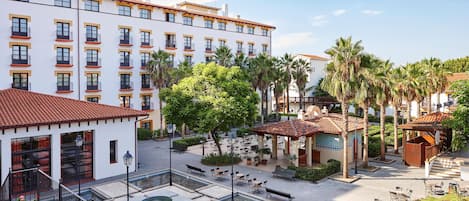 A hotel courtyard with outdoor seating, palm trees, and a pool area.