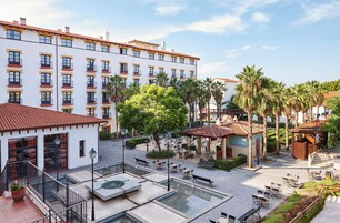 A hotel courtyard with outdoor seating, palm trees, and a pool.