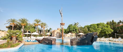 Piscina con dos barcos, sillas de descanso y palmeras.