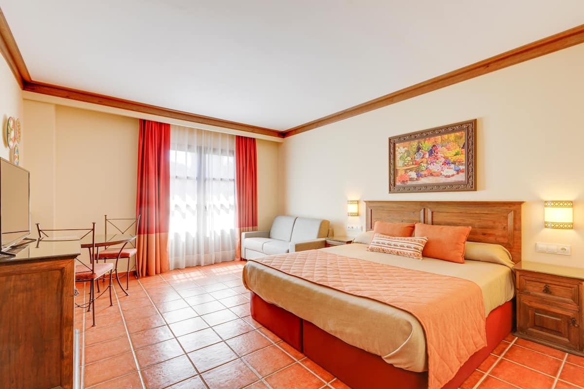 Habitación de hotel con cama, escritorio, silla, sofá y un cuadro en la pared.