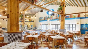 Un restaurante espacioso con altos vigas de madera, suelo de baldosas de cuadros y sillas de mimbre. Las mesas están preparadas con manteles blancos y copas de vino.