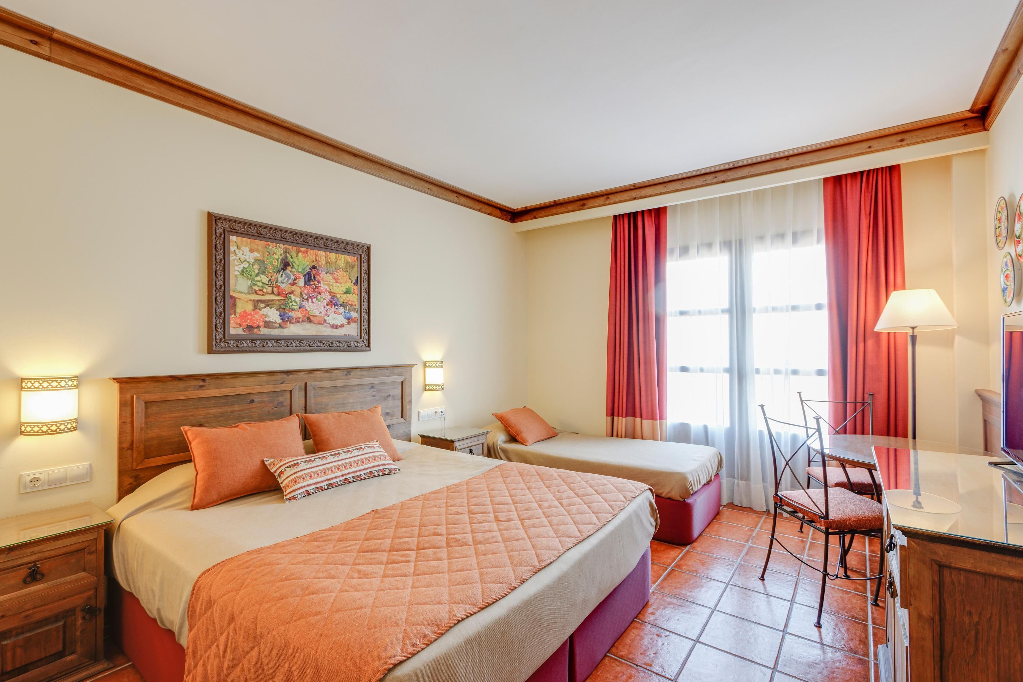 Une chambre d’hôtel avec un grand lit, deux petits lits, un bureau avec une chaise et un tableau au mur.