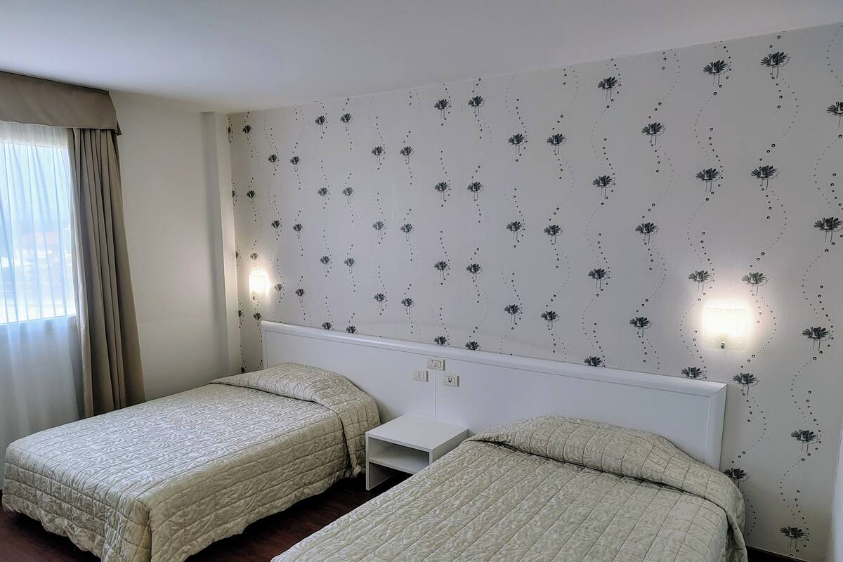 A hotel room with two beds, a nightstand, and a wall with a floral pattern.