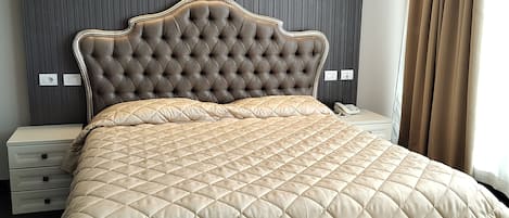 A large bed with a tufted headboard, a bedside table, and a nightstand.