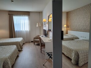 A hotel room with two single beds, a desk with a chair, a desk lamp, a telephone, and a mirror.