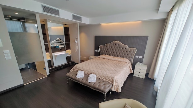 Habitación de hotel moderna con una cama grande, un tocador con espejo, un aparador y un área de descanso con una silla y una mesita.