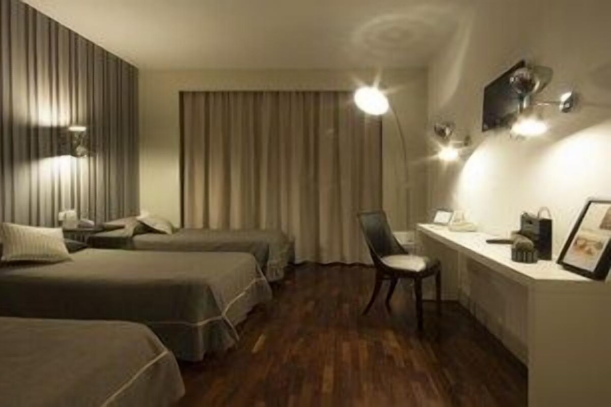 A hotel room with two beds, a desk, a chair, and a large window with curtains.