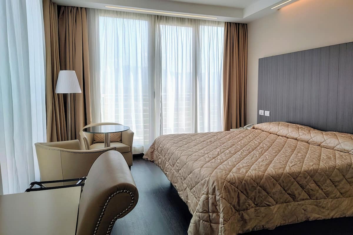 A hotel room with a bed, a chair, a small table, and a lamp.