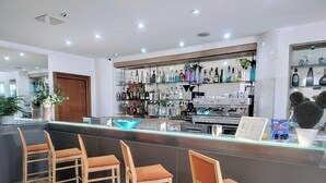 Zona de bar con sillas de madera, un expositor de vidrio y una variedad de botellas y vasos.