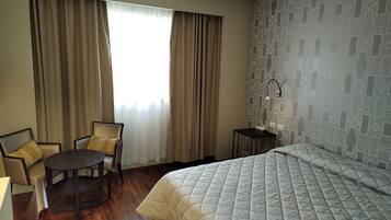 Ein Hotelzimmer mit einem Bett, einem runden Tisch mit Stühlen, einem kleinen Nachttisch mit Lampe und einer Wand mit Muster.