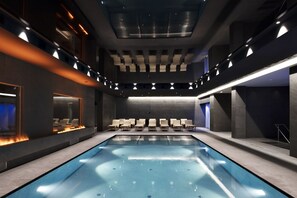 A modern indoor swimming pool with a long, narrow shape, surrounded by seating areas and a high ceiling with recessed lighting. - Grand Hotel Duca D'Este (Tivoli)