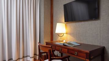 Habitación de hotel con escritorio de madera, lámpara, televisor de pantalla plana en la pared y ventana con cortinas.