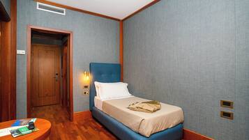 Una habitación de hotel con una cama azul, suelo de madera y una pequeña mesa con folletos.