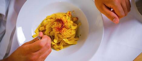 A person holding a white plate with pasta, a bottle of wine, and a glass of red wine on a table.