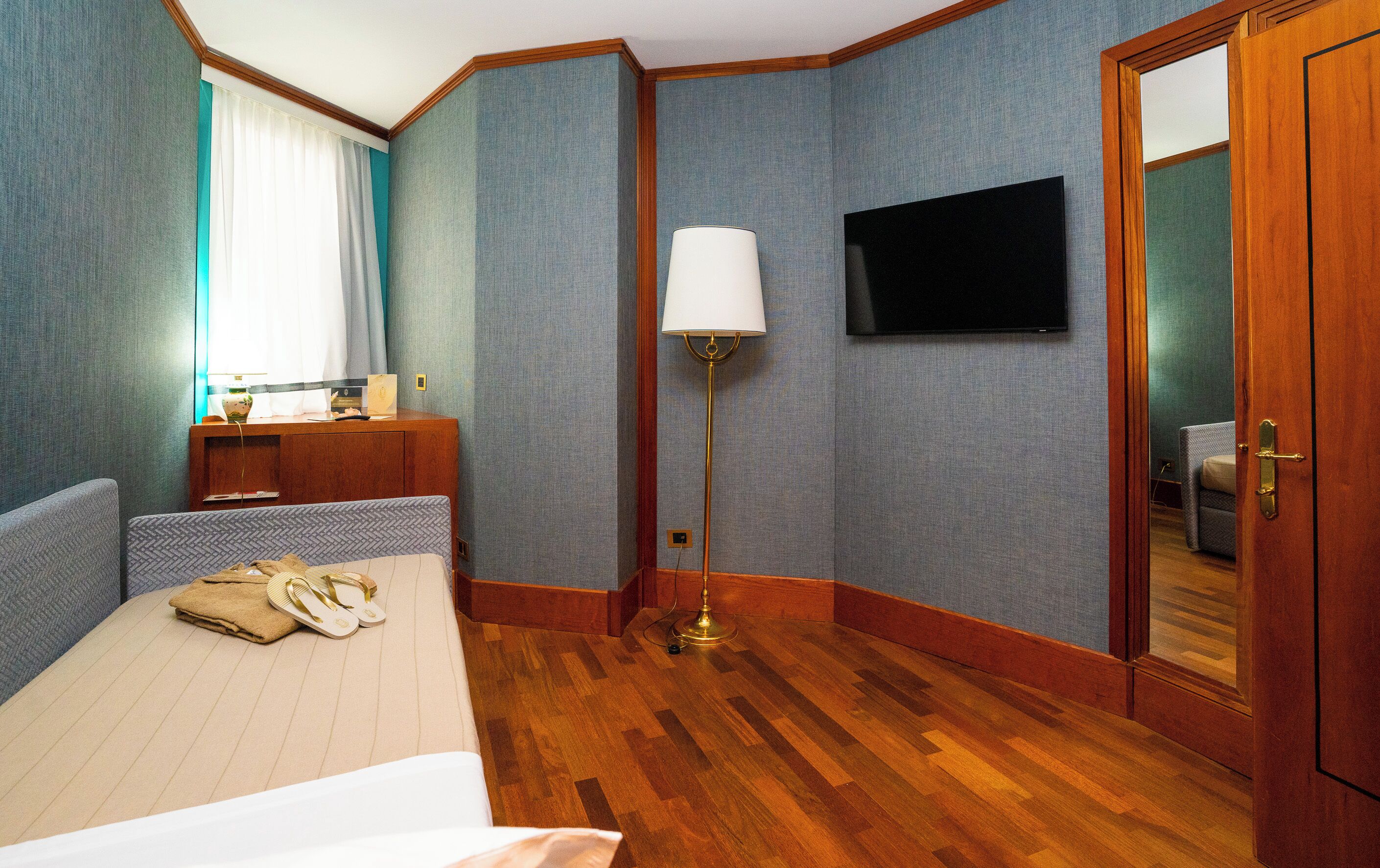 Una habitación de hotel con cama, escritorio, lámpara, televisor y puerta.
