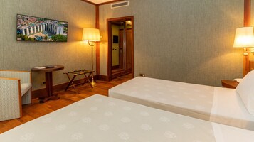Habitación de hotel con dos camas, un escritorio, una silla, una mesita y un cuadro de un edificio.