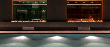 A swimming pool with a fire feature and a glass enclosure.
