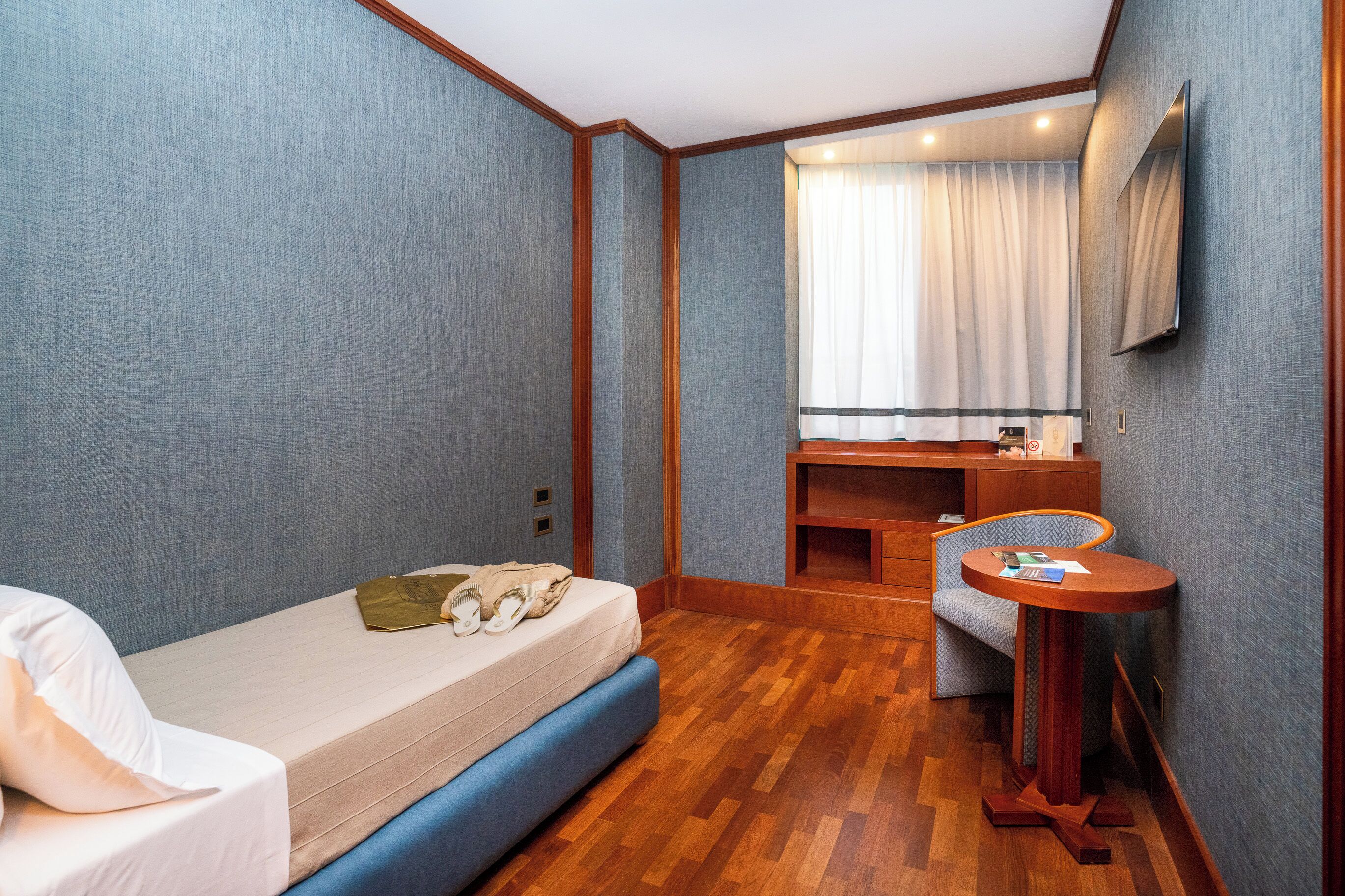 Habitación de hotel pequeña con una cama individual, un escritorio, una silla y un espejo.