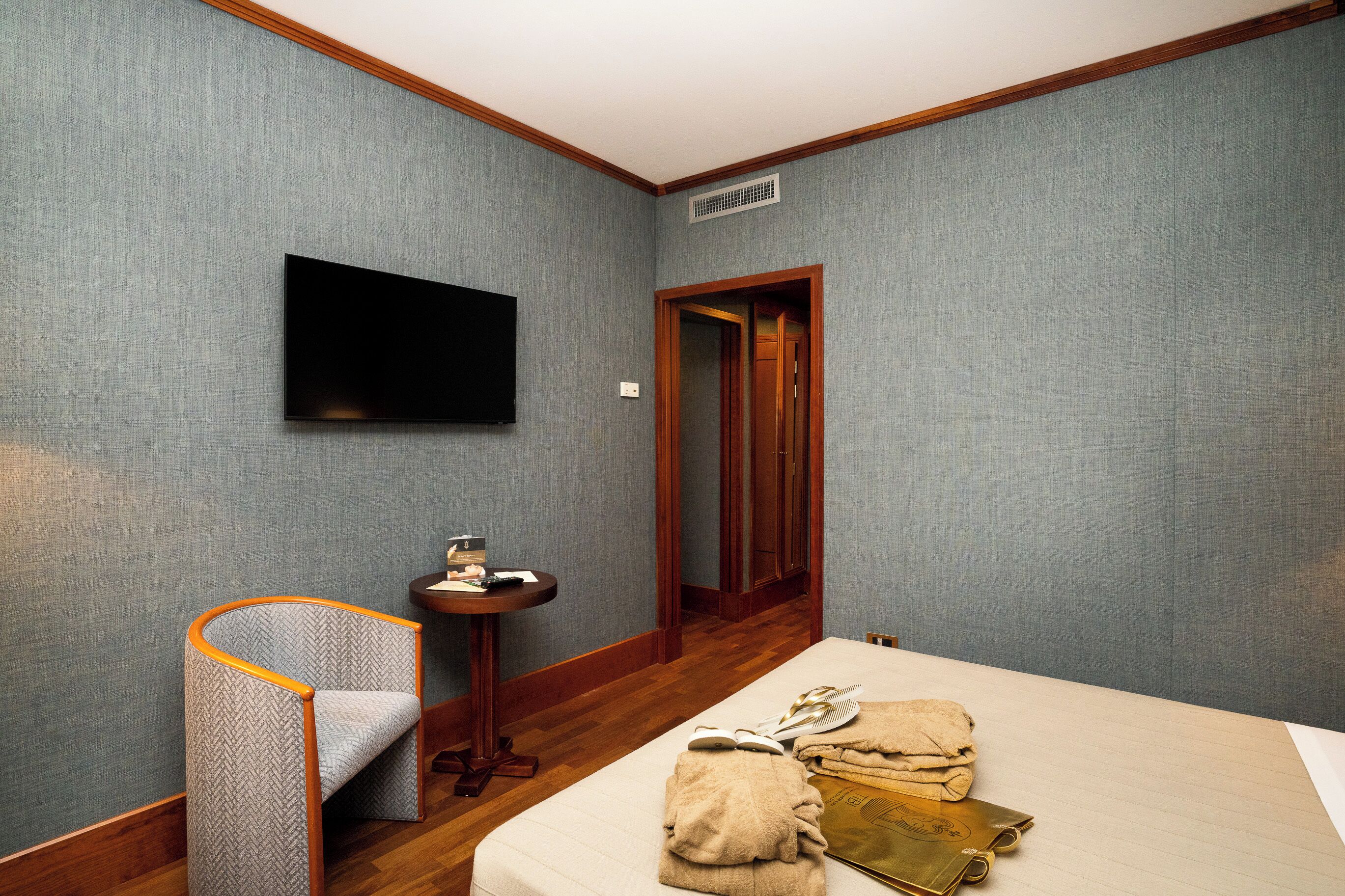 A hotel room with a bed, a chair, a small table, and a television mounted on the wall.