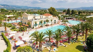 Un resort con una piscina grande, palmeras y vistas a montañas distantes.