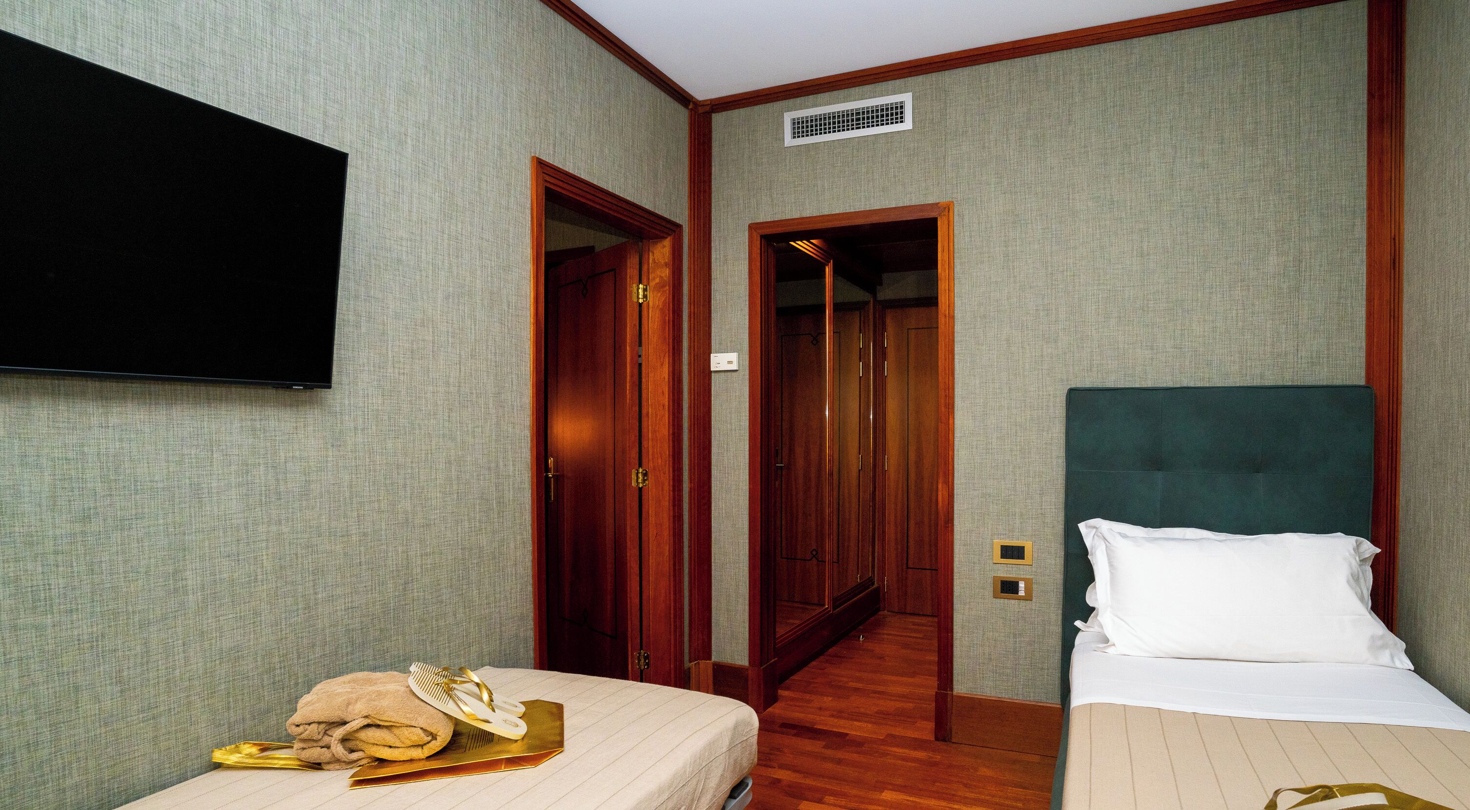 A hotel room with two beds, a television, and a hallway leading to another room.