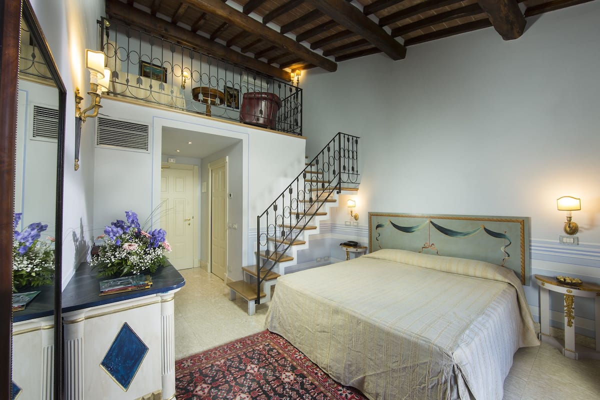 A bedroom with a large bed, a wooden staircase, and a small table with a lamp.