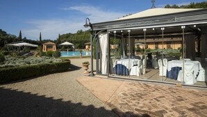 A covered outdoor dining area with tables and chairs, a pool, and a garden in the background. - Hotel Il Piccolo Castello (Monteriggioni)