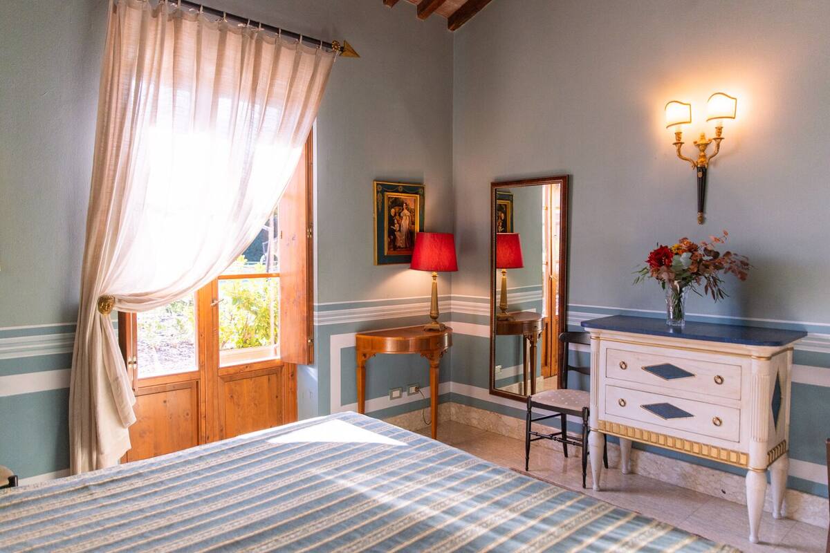 A bedroom with a bed, a vanity with a mirror, a dresser, and a window with curtains.