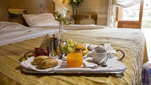 A neatly made breakfast tray on a bed with a tray of bread, fruit, juice, and tea, in a room with a bed, curtains, and a painting on the wall. - Hotel Il Piccolo Castello (Monteriggioni)