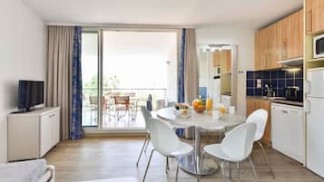 A modern kitchen with white cabinets, a dining table with chairs, and a balcony with a view.