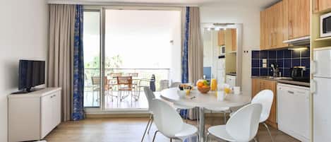 A modern kitchen with white cabinets, a dining table with chairs, and a balcony with a view.