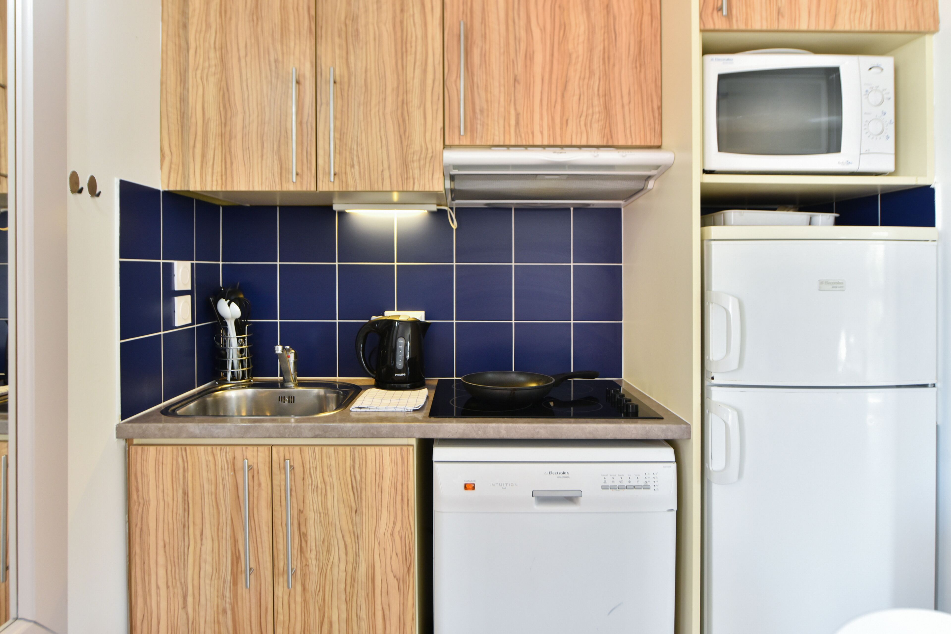 A compact kitchen with wooden cabinets, a microwave, a white refrigerator, and a dishwasher.