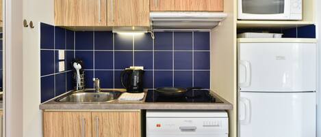 A compact kitchen with wooden cabinets, a microwave, a white refrigerator, and a dishwasher.