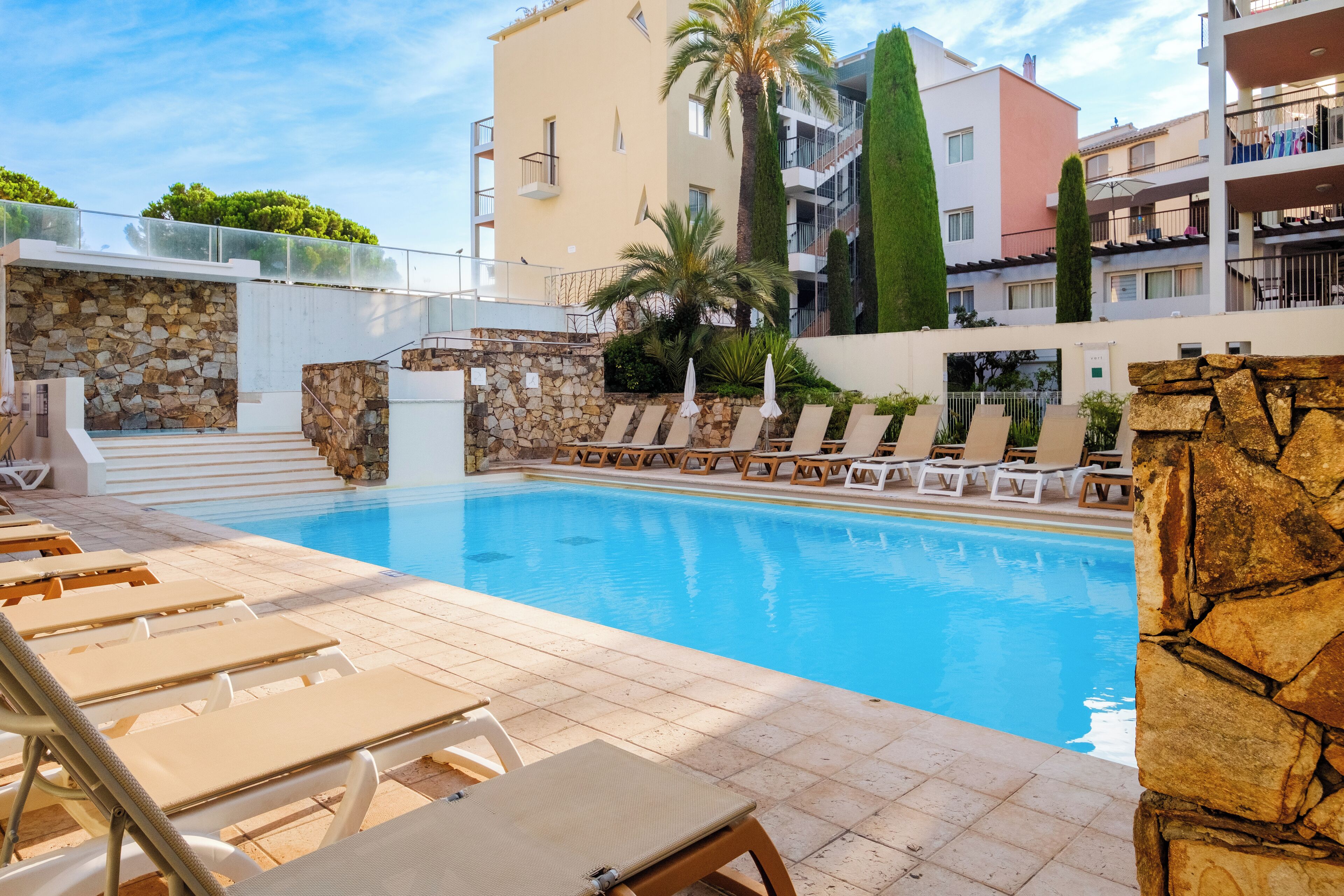 Una piscina con lettini, un muro in pietra e una scala che conduce a un livello superiore.