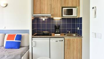 A compact kitchenette with wooden cabinets, a microwave, a coffee maker, and a dishwasher.