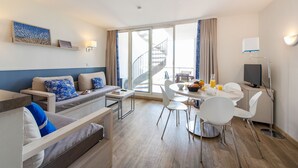 A modern hotel room with a sofa, dining table, chairs, a TV, and a staircase leading to an outdoor area. - Résidence Pierre & Vacances Premium Port-Prestige (Antibes)