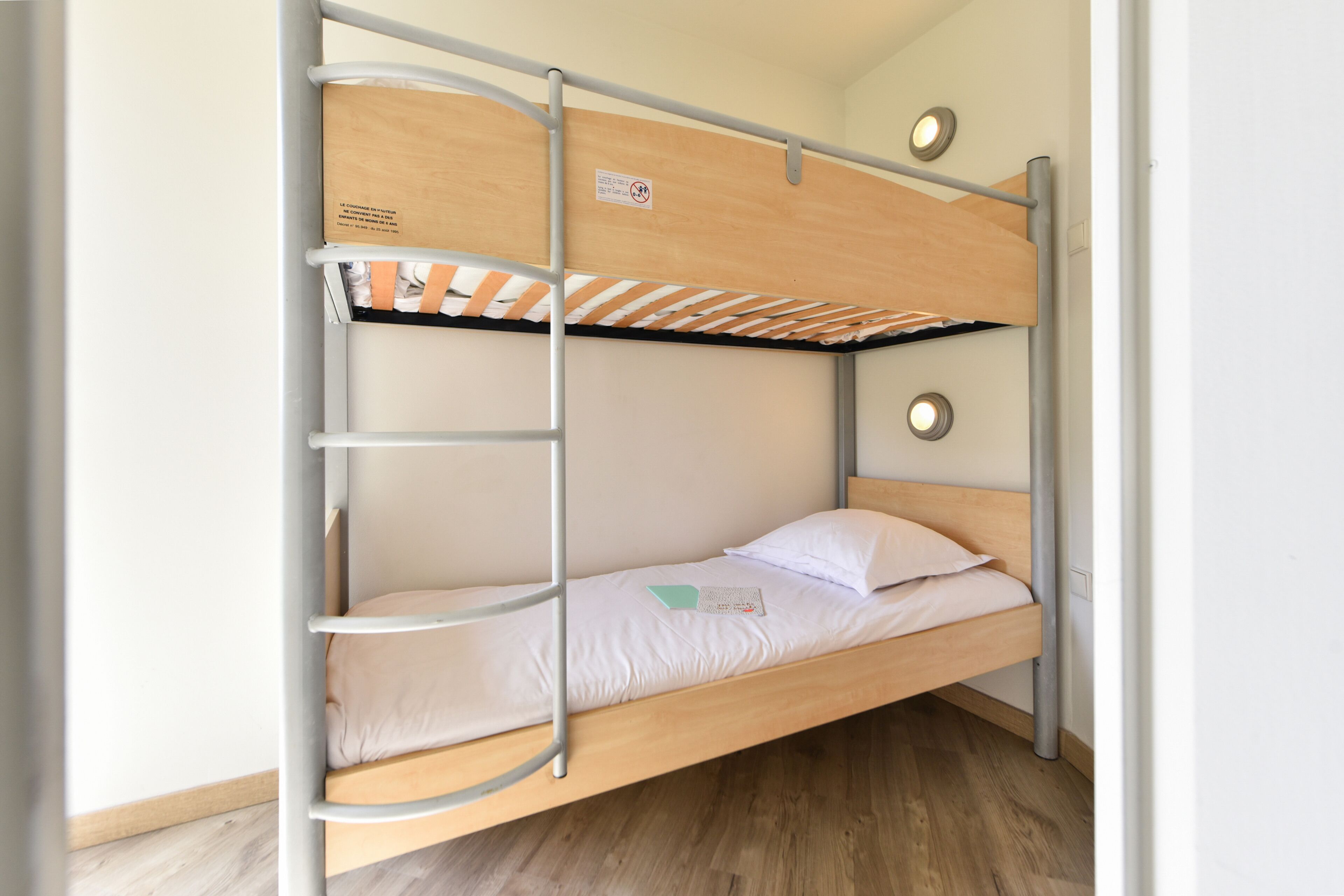 Ein Stockbett mit einer Leiter, einem Holz-Kopfstück und einer weißen Matratze.