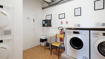 A laundry room with a washing machine, a dryer, a chair, a fire extinguisher, and a control panel.