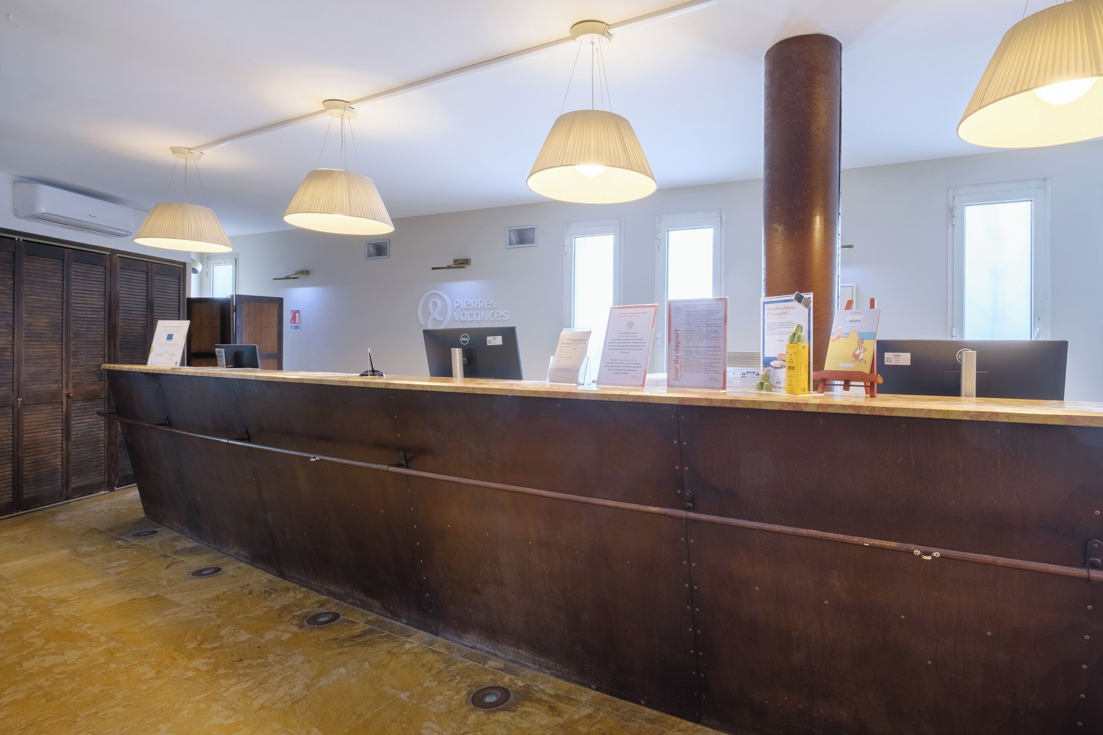 A reception desk with a wooden counter, multiple pendant lights, and a large cylindrical column.