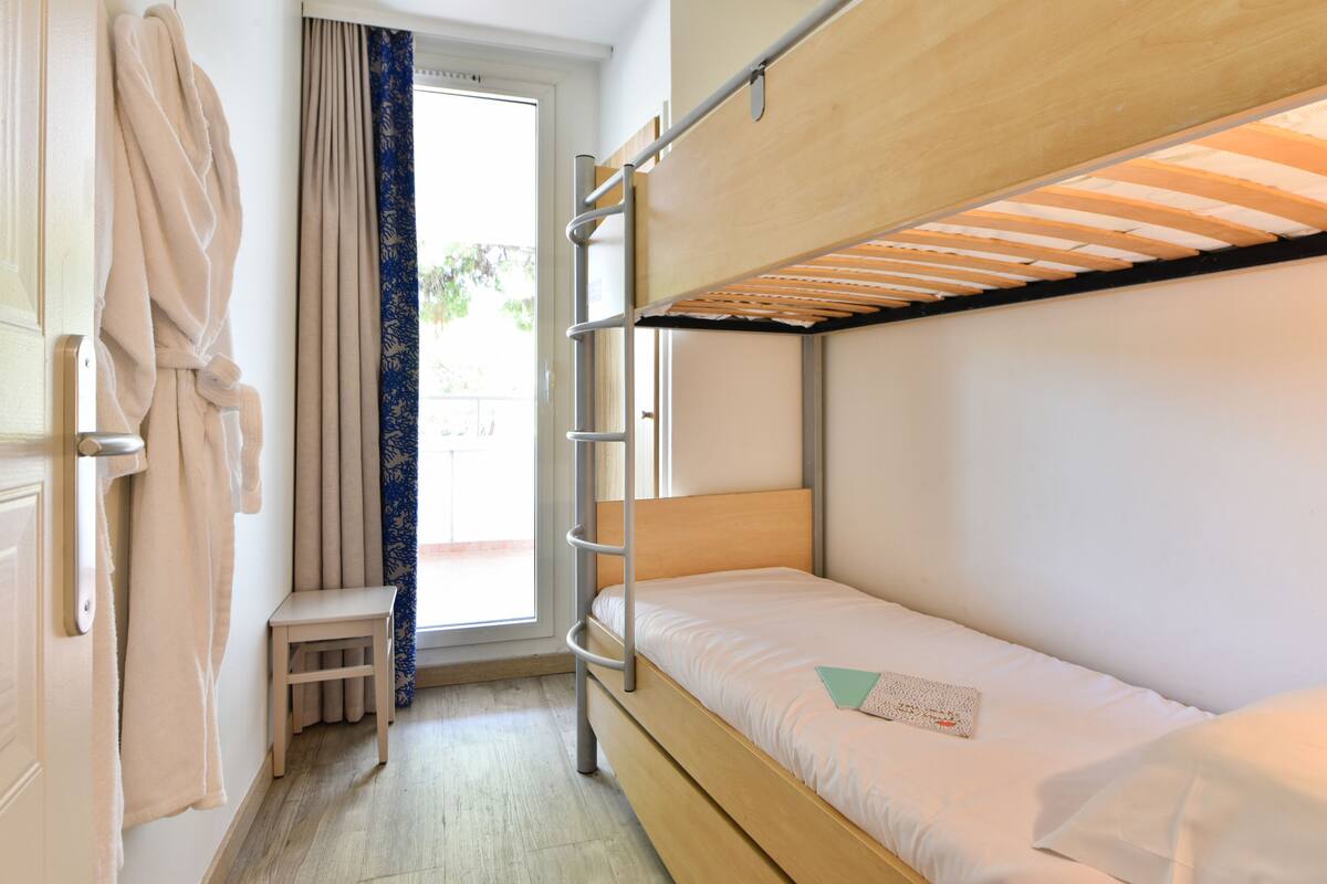 A bunk bed room with a wooden ladder, a small stool, and a window with curtains.
